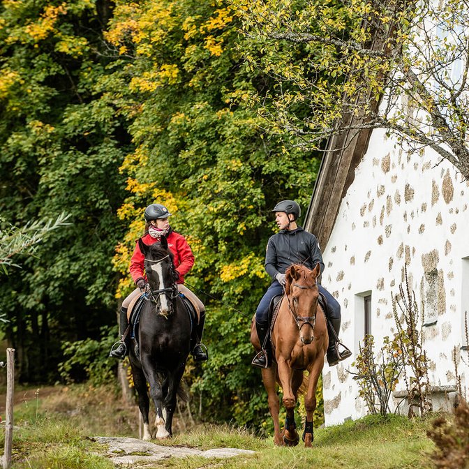 Wanderreiter vor einem Waldrand und neben einem Stoabloss Haus